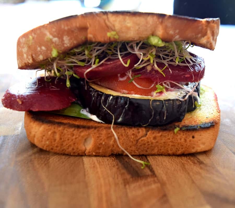 eggplant, tomatoes and sprouts on a sandwich on wooden cutting board