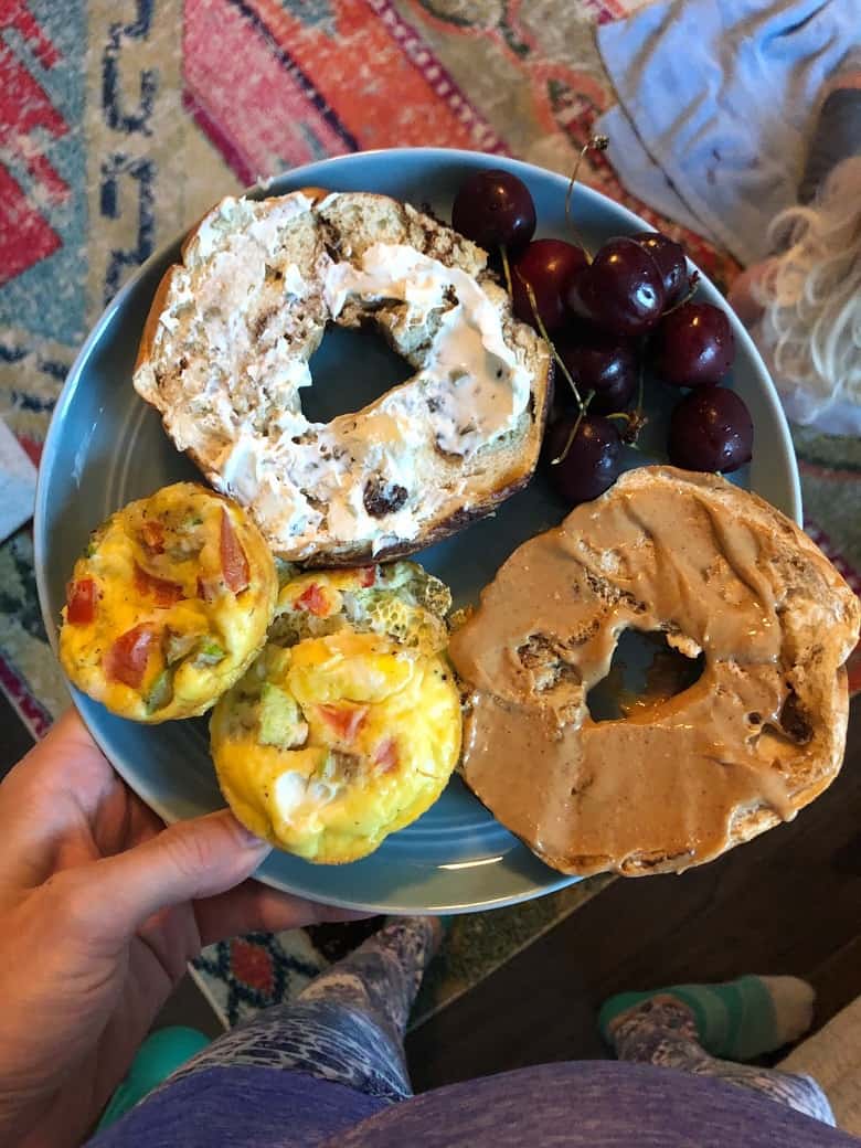 blue plate with bagel with cream cheese and peanut butter, cherries and egg muffins