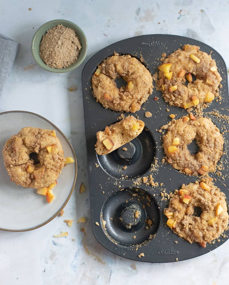 whole wheat donuts in donut plan with peach crumble topping and donut on plate next to donut pan