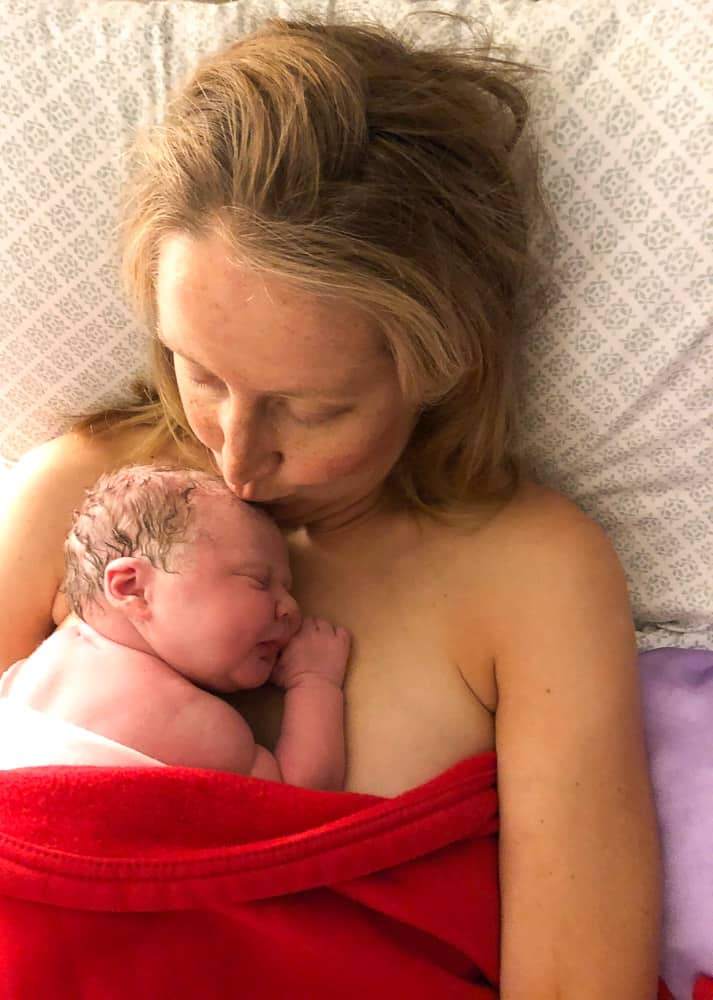 mom kissing newborn baby in bed