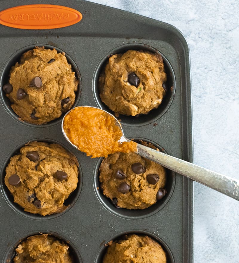 whole wheat pumpkin muffins in muffin tin with spoon of pumpkin puree