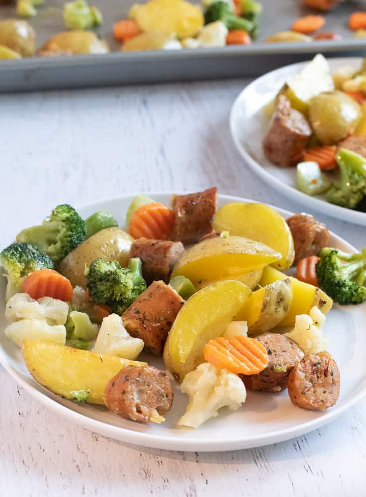 white plate with yellow potatoes, sliced chicken sausage and veggies