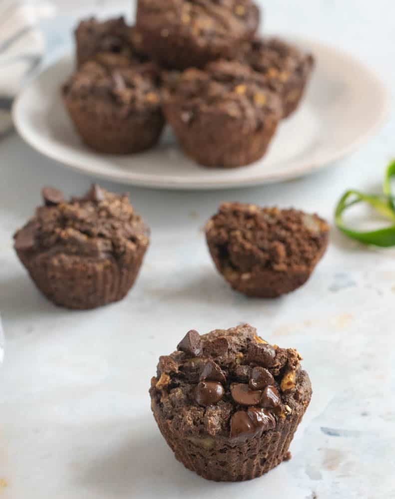 gluten free chocolate zucchini muffins on white countertop with bowl of more muffins in background