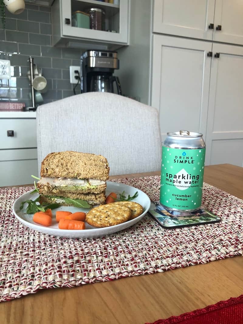 Drink Simple Cucumber Maple Water can next to plate with sandwich on it on table