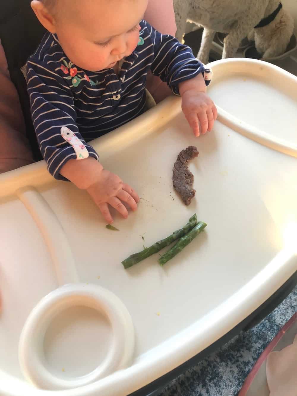 6 month old baby eating beef and asparagus in high chair