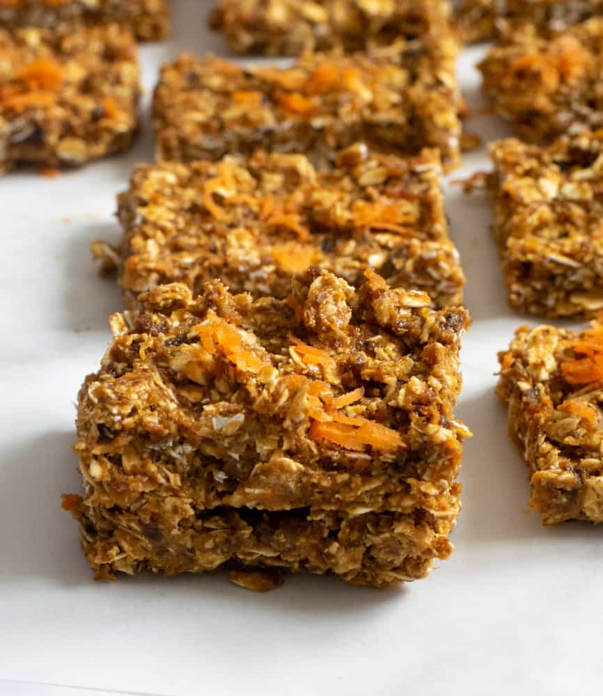 closeup of no bake vegan carrot cake bars on parchment paper topped with shredded carrot