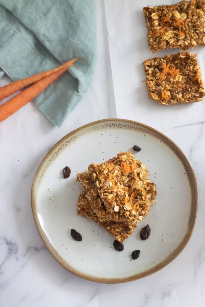 no bake carrot cake bars cut into squares on gray plate with gold lining and raisins on plate