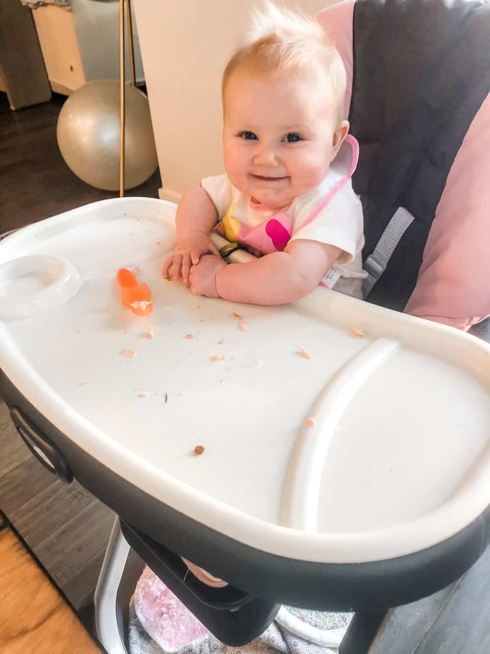 6 month old baby smiling while eating solids with gootensil