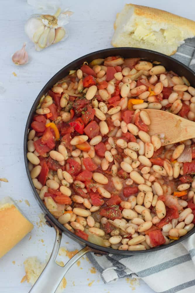 skillet with white northern beans, canned tomatoes and wooden spoon to stir