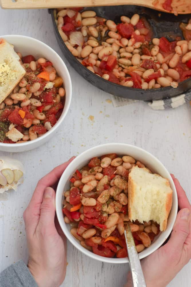 Cannellini Bean Skillet Recipe served in white bowl with bread with person holding bowl