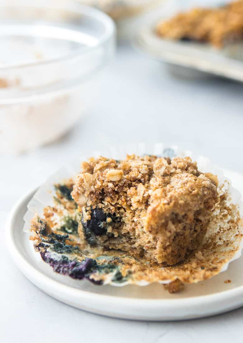 blueberry muffin with crumb topping in muffin wrapper on white plate