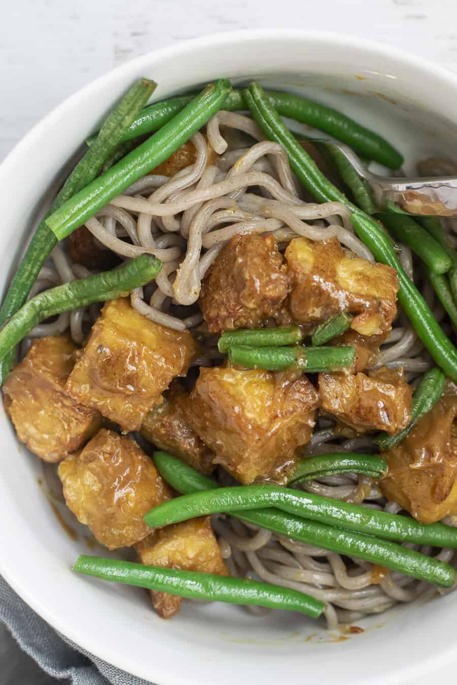 bowl of rice noodles with air fried tempeh in tempeh peanut sauce and green beans