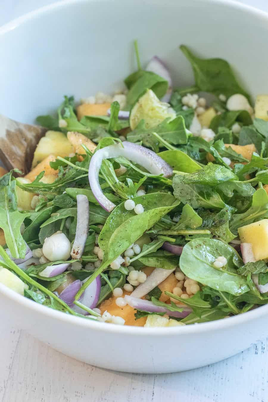 Cantaloupe salad served atop arugula and greens in white serving bowl